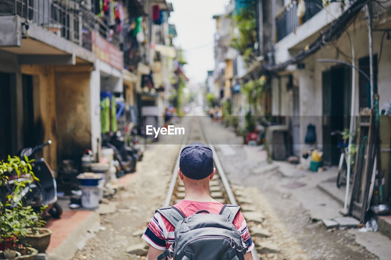 Rear view of man with backpack standing on railroad track amidst houses