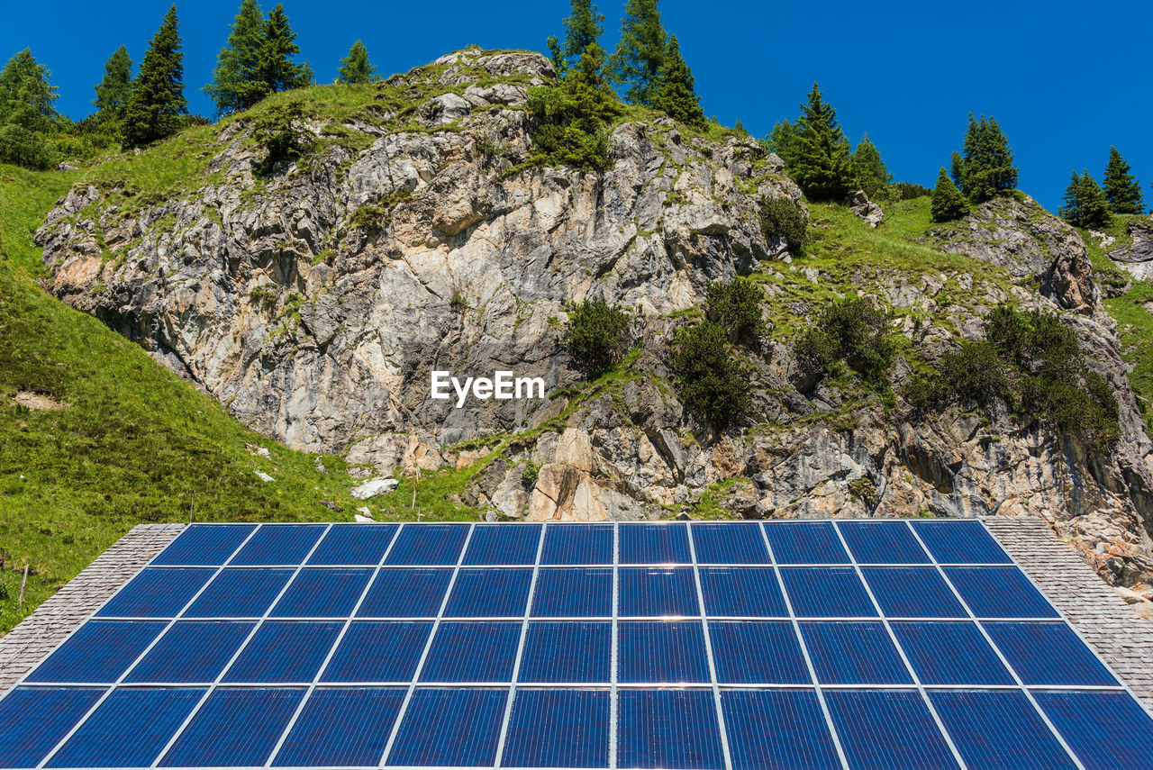 Solar photovoltaic panels against the backdrop of rocky mountains covered with green plants trees