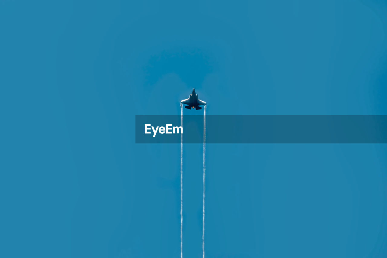 Low angle view of airplane flying against clear blue sky