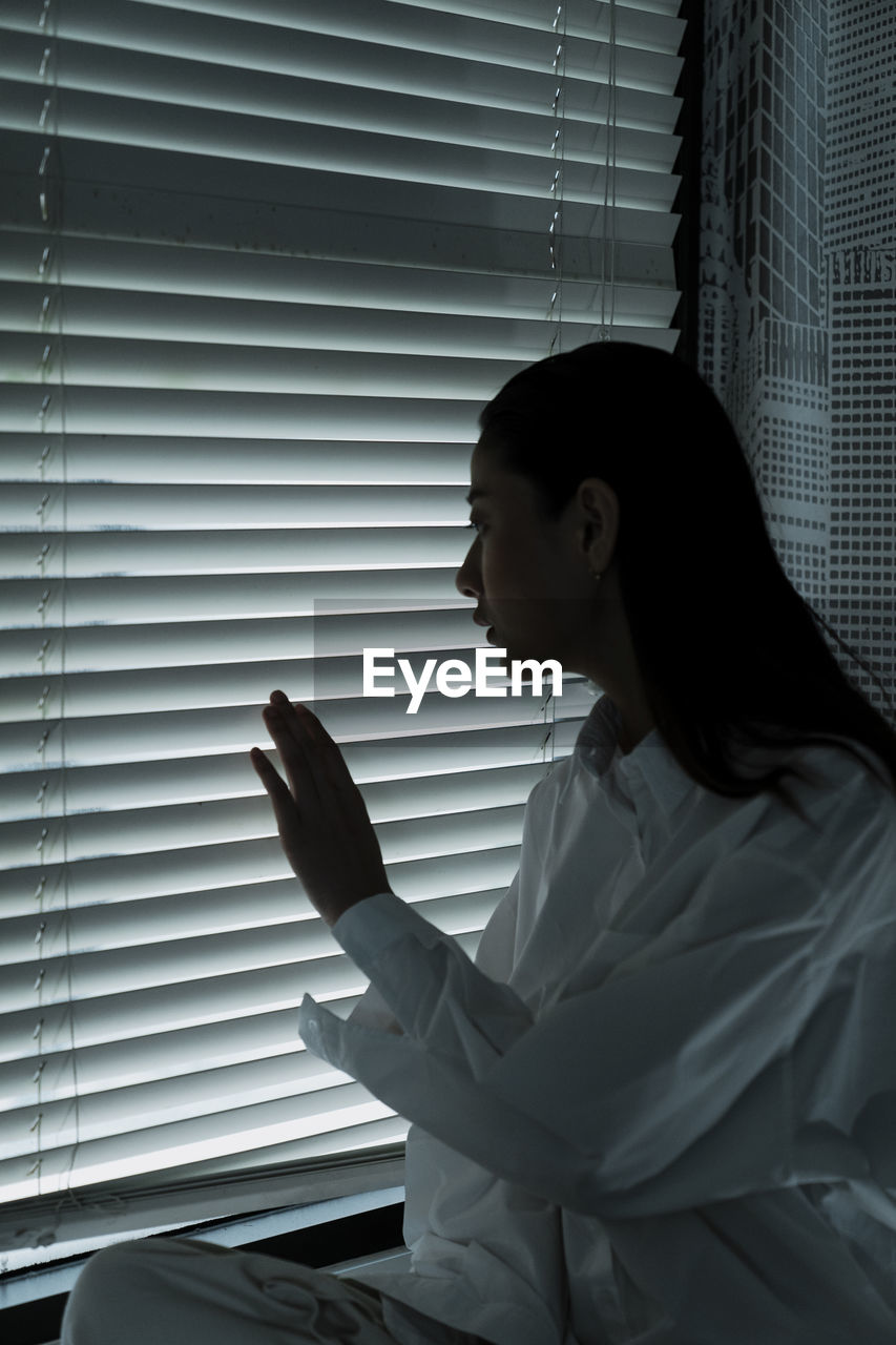 SIDE VIEW OF YOUNG WOMAN LOOKING THROUGH WINDOW