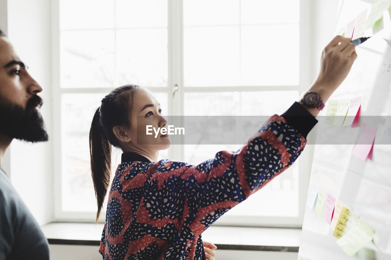 Female engineer writing on whiteboard and explaining colleague in office