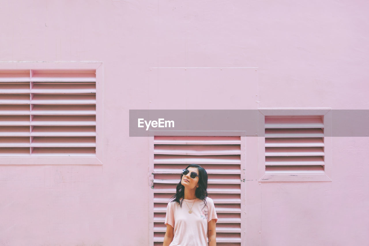 Woman with sunglasses standing against pink wall