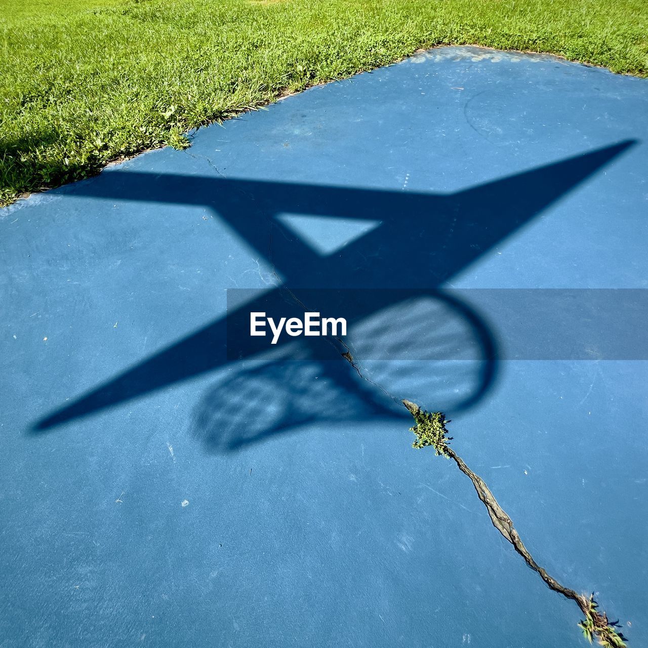 Shadow of basketball hoop on cracked blue court.