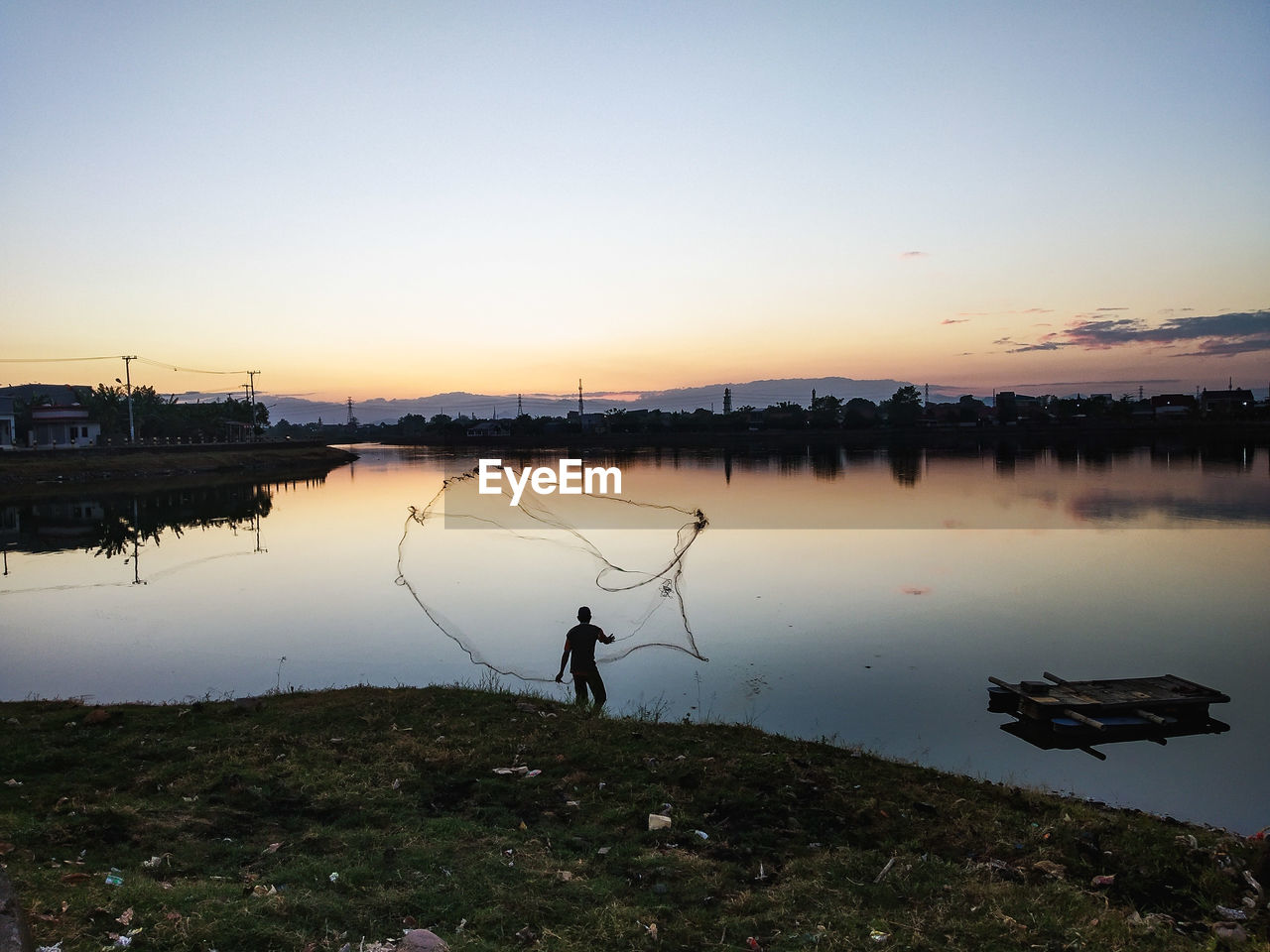 Fisherman holding fishing net by lake during sunset