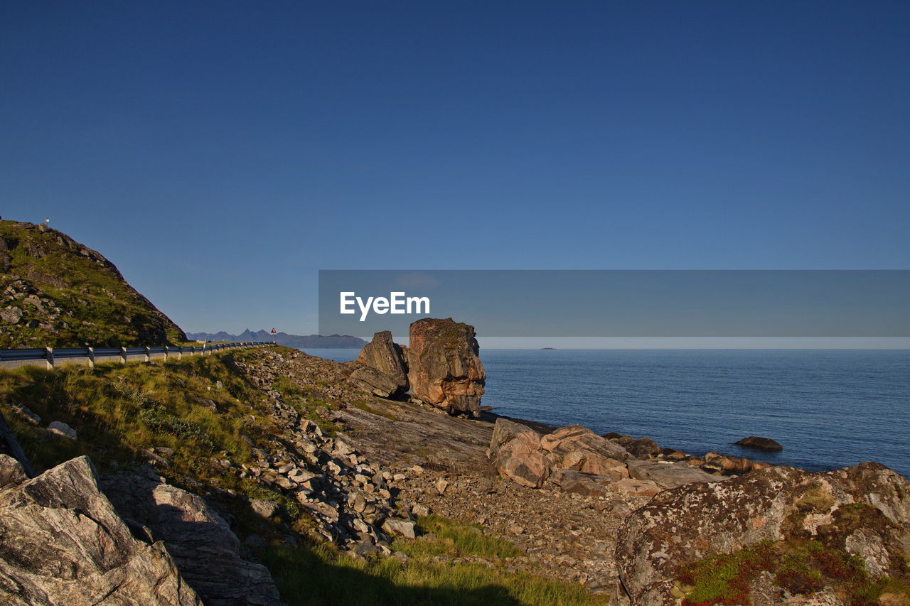 Rock formations by sea against clear blue sky