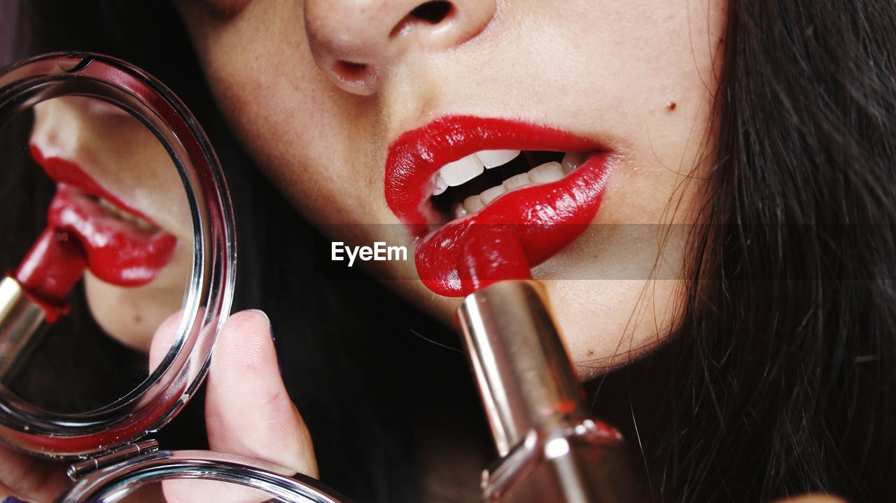 Close-up midsection of woman applying red lipstick 