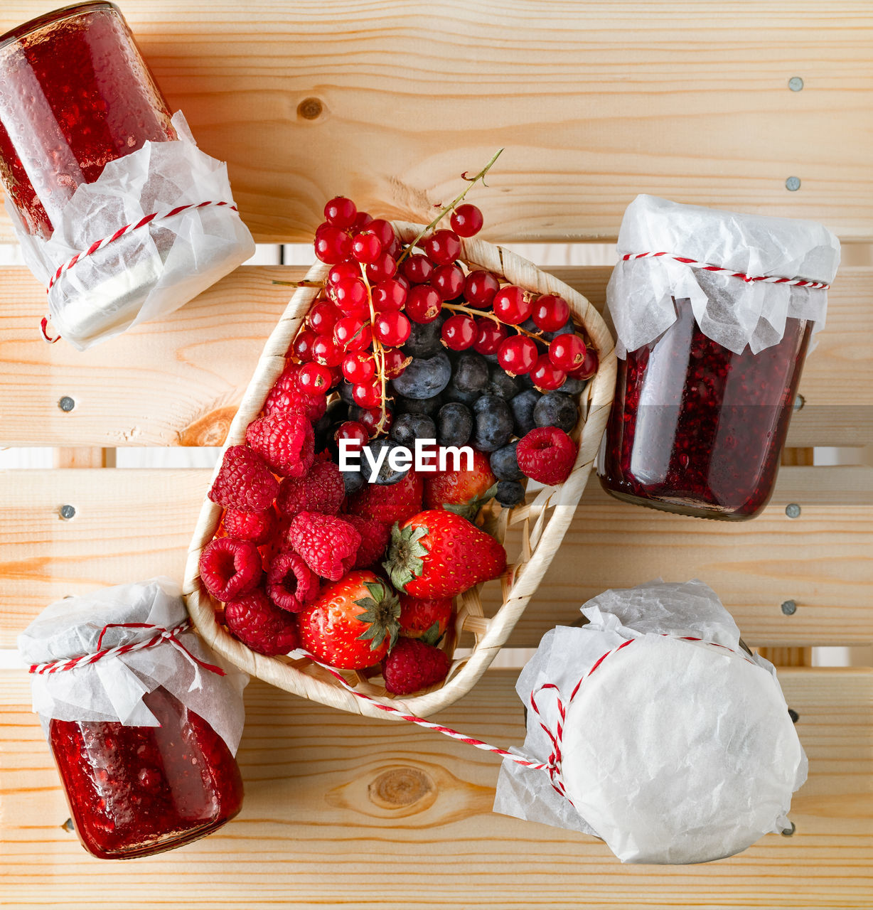 Assorted fresh berries, homemade jams in glass jars on wooden background, top view