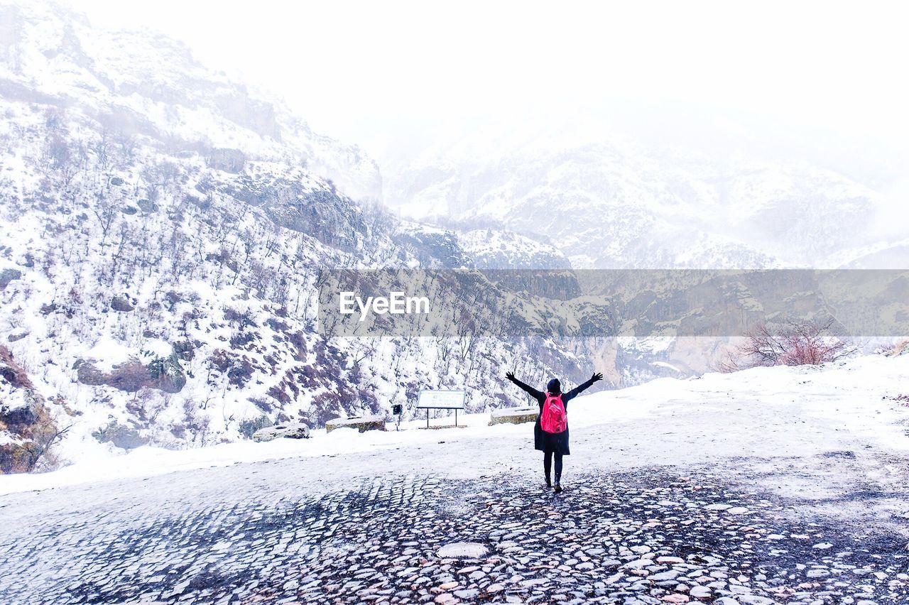 Rear view of person standing on snow covered field against mountains