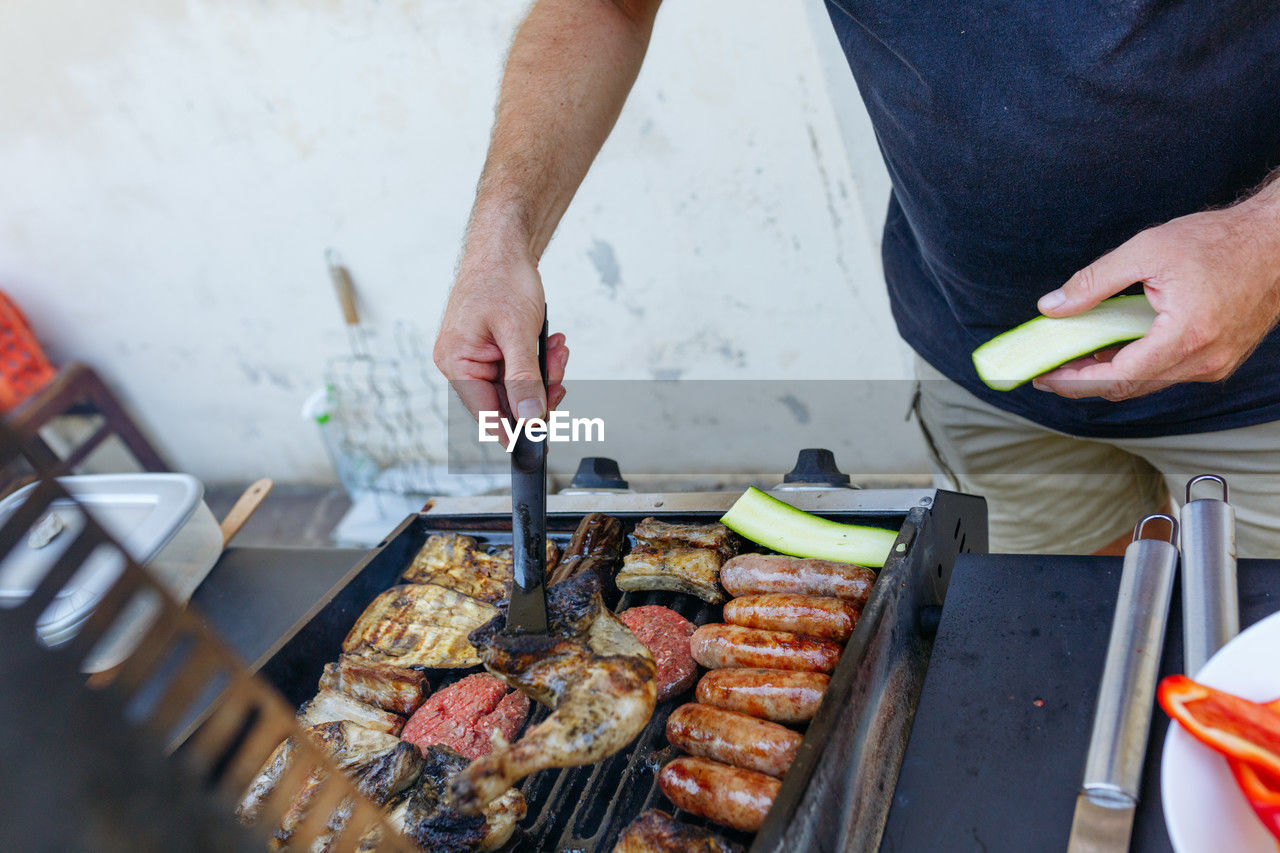 Upper view of man cooking vegetables and meat on a grill in the garden