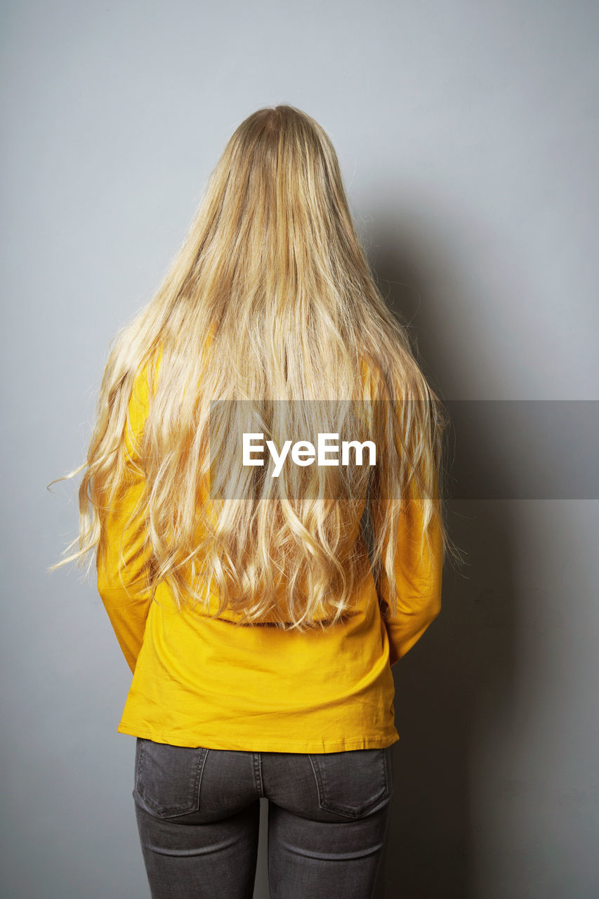 Rear view of teenage girl with blond hair standing against gray background