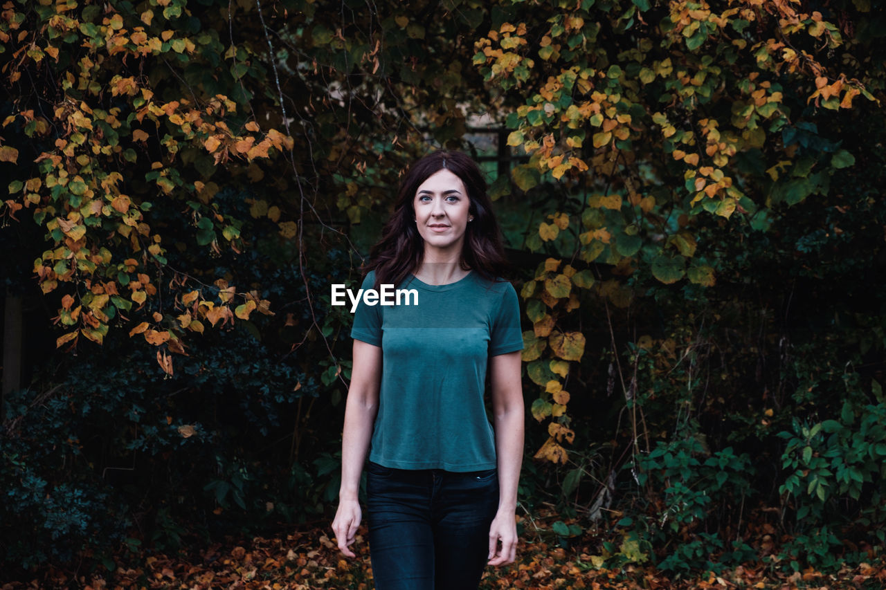 PORTRAIT OF BEAUTIFUL YOUNG WOMAN STANDING AGAINST TREES