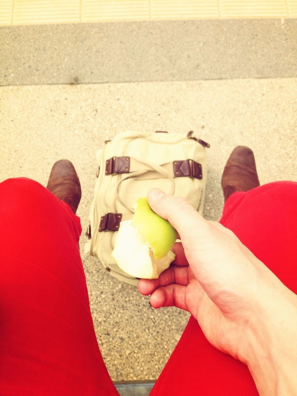 Low section of person in red pants eating a fruit