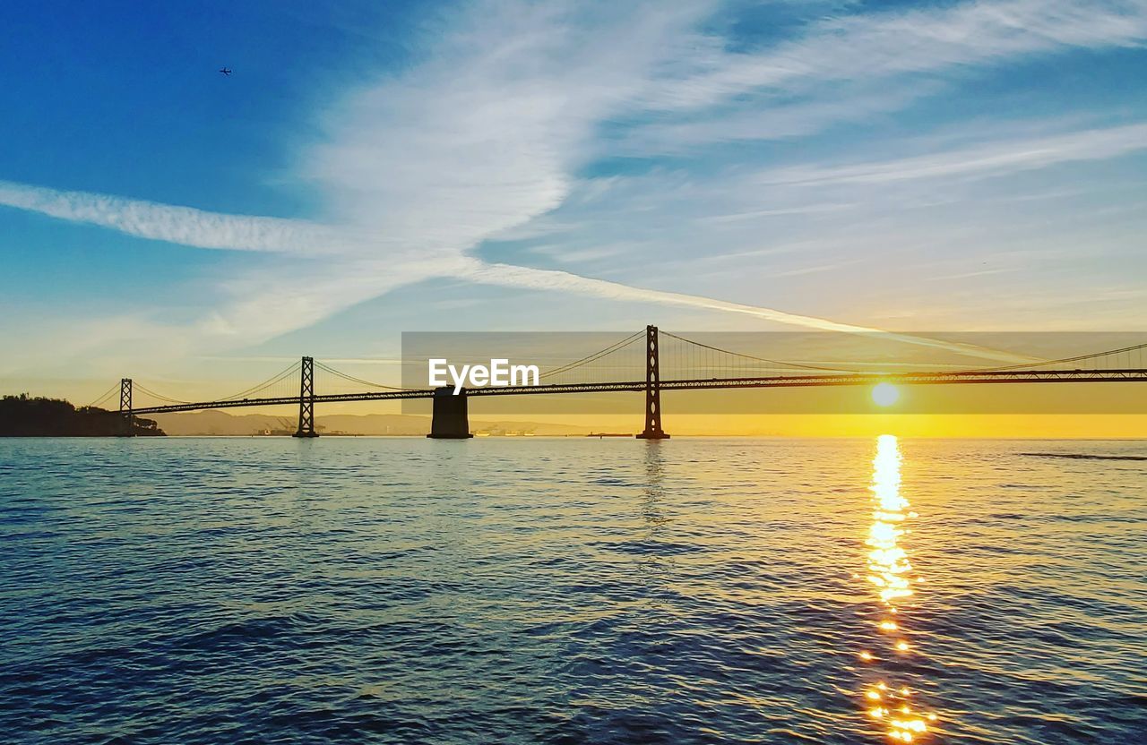 VIEW OF SUSPENSION BRIDGE OVER SEA DURING SUNSET