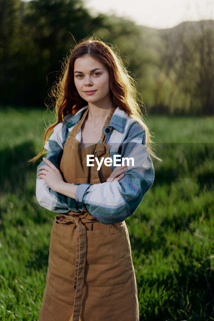 Portrait of smiling young farmer with arms crossed in front of plants