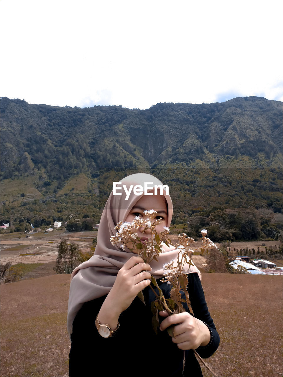 Portrait of woman in hijab holding flowers on field