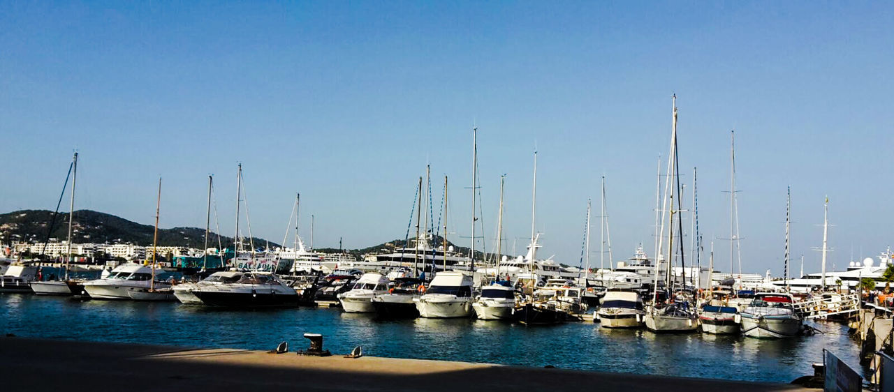 Sailboats moored at harbor against clear sky