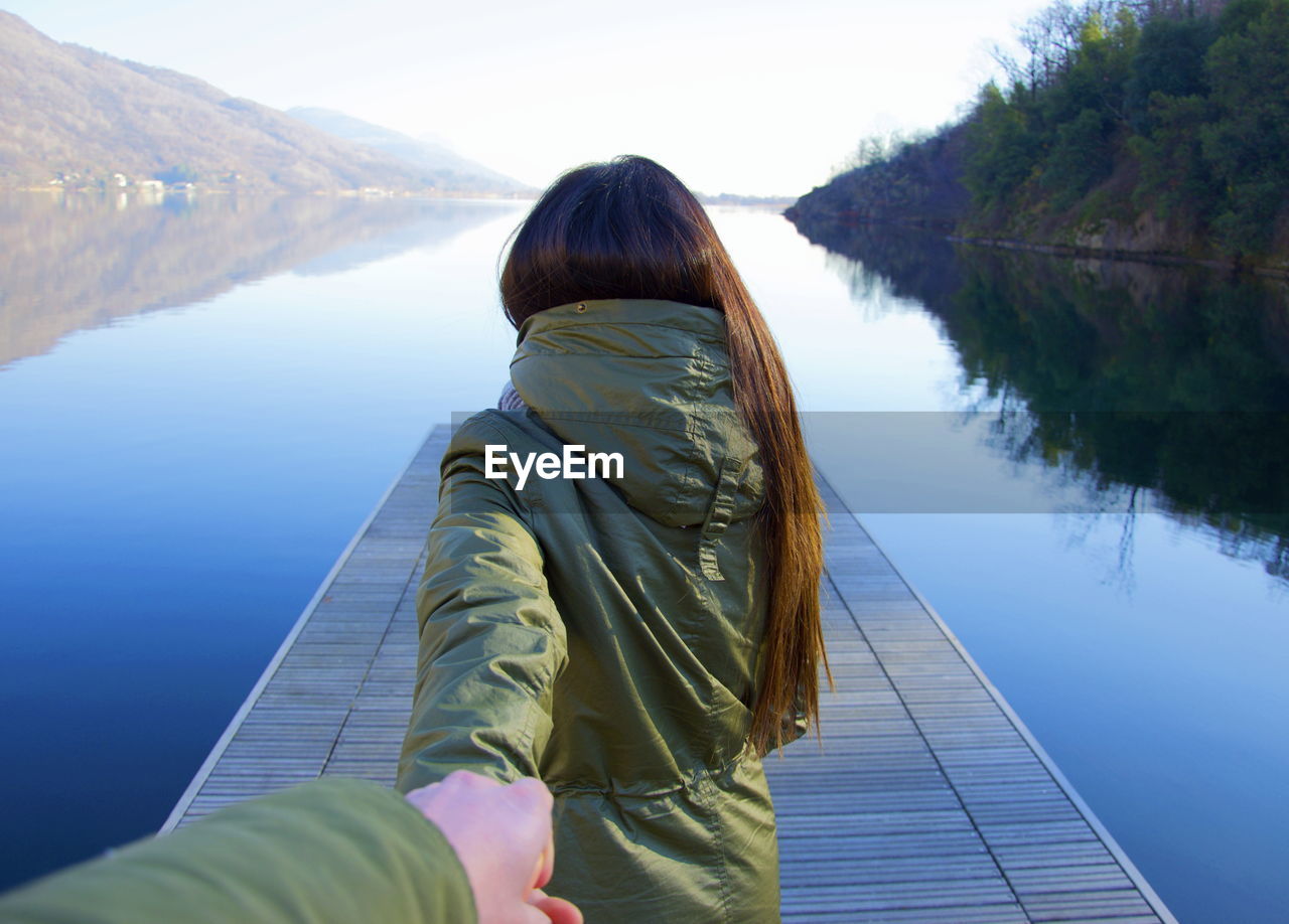 Cropped image of man holding girlfriend hand on jetty over river