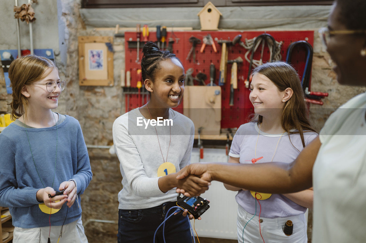 Smiling female student doing handshake with teacher during technology workshop at school