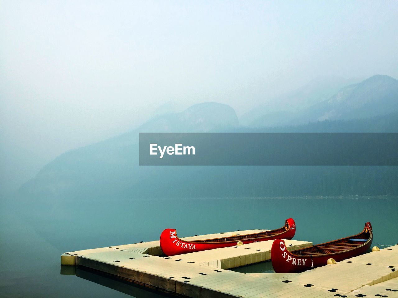 Red boats moored at pier on lake louise during foggy weather