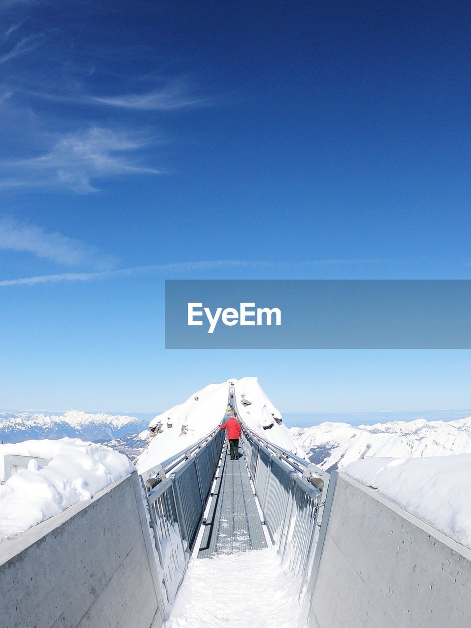 Rear view of people walking on footbridge at snow covered mountains against sky