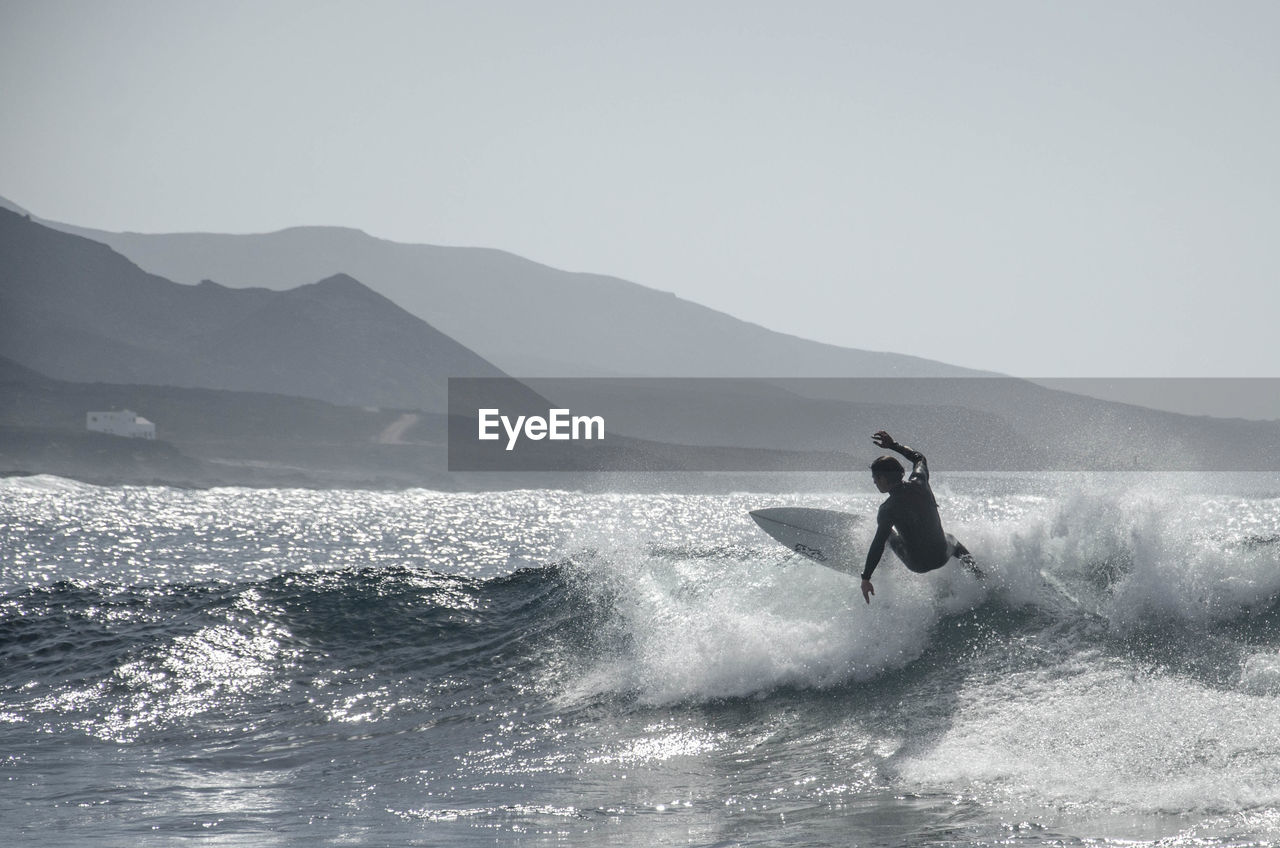 Full length of man surfing in sea against mountains