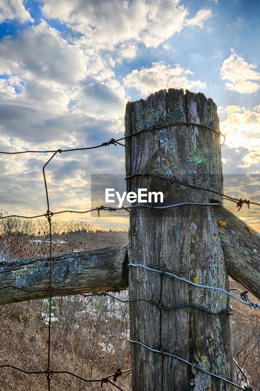 CLOSE-UP OF WOODEN POST AGAINST CLOUDY SKY