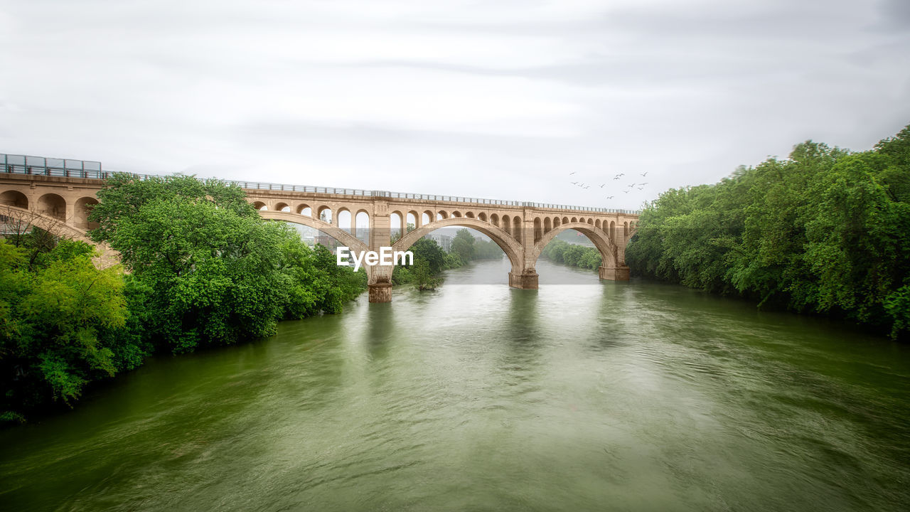 ARCH BRIDGE OVER RIVER BY TREES AGAINST SKY