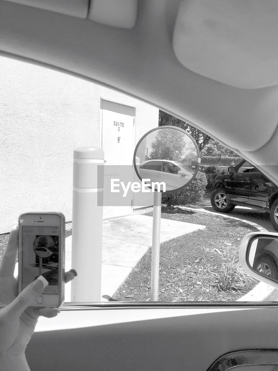 Cropped image of woman photographing traffic mirror through smart phone in car