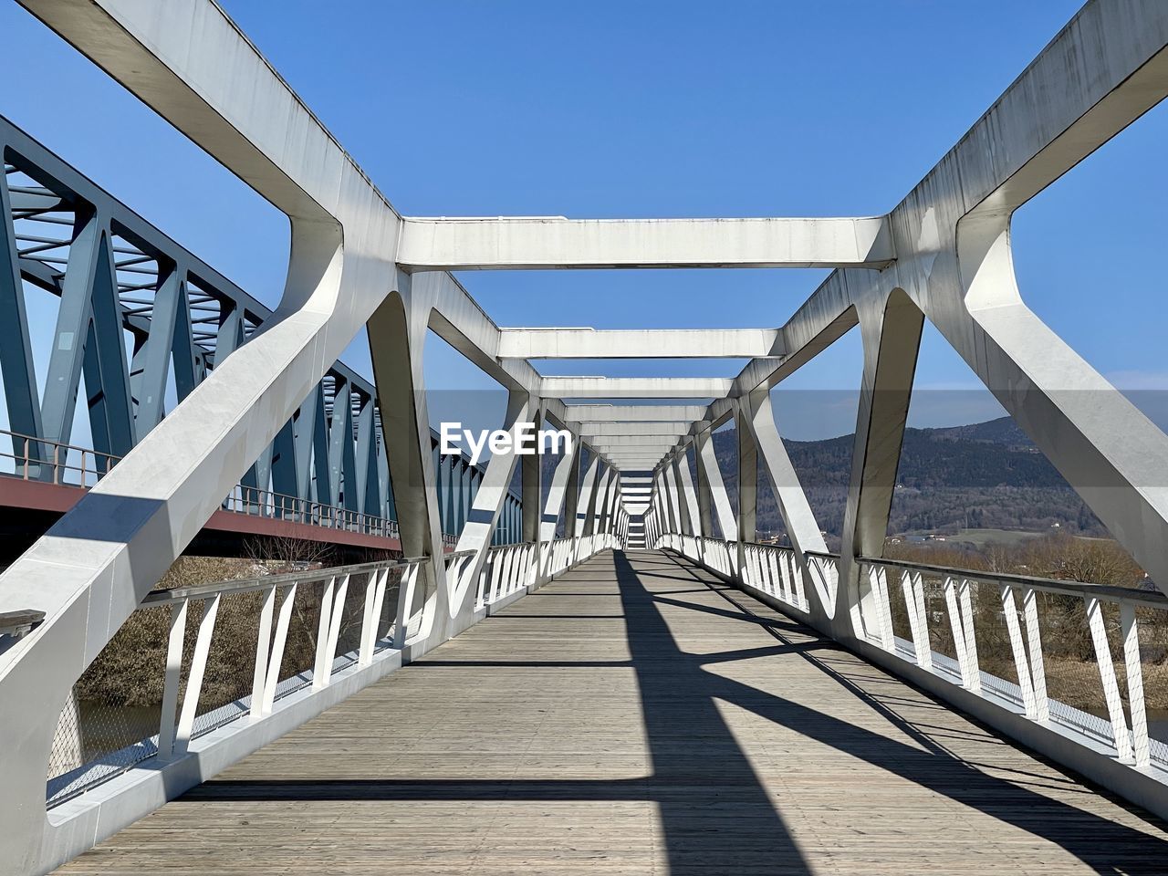 architecture, built structure, bridge, sky, nature, sunny, sunlight, transportation, clear sky, walkway, no people, blue, day, city, shadow, travel destinations, water, outdoors, footpath, diminishing perspective, the way forward, travel, wood, overpass