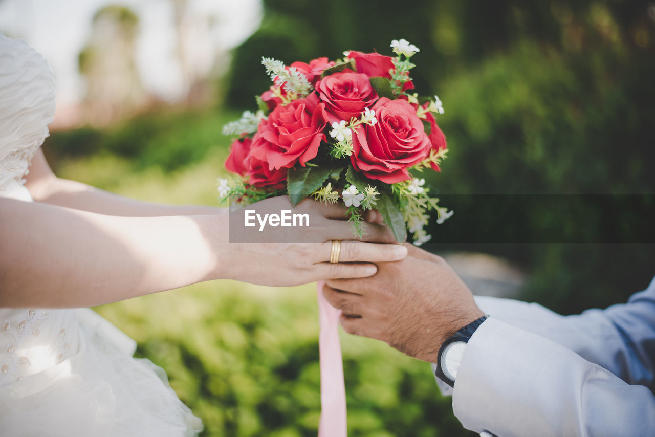 Midsection of groom giving bouquet to bride during wedding ceremony