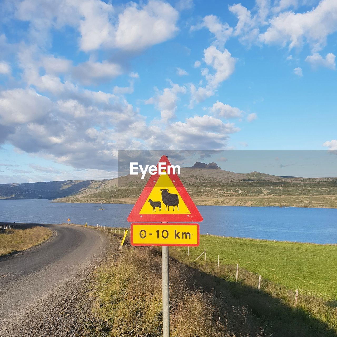 Animal crossing sign at roadside with lake in background against sky