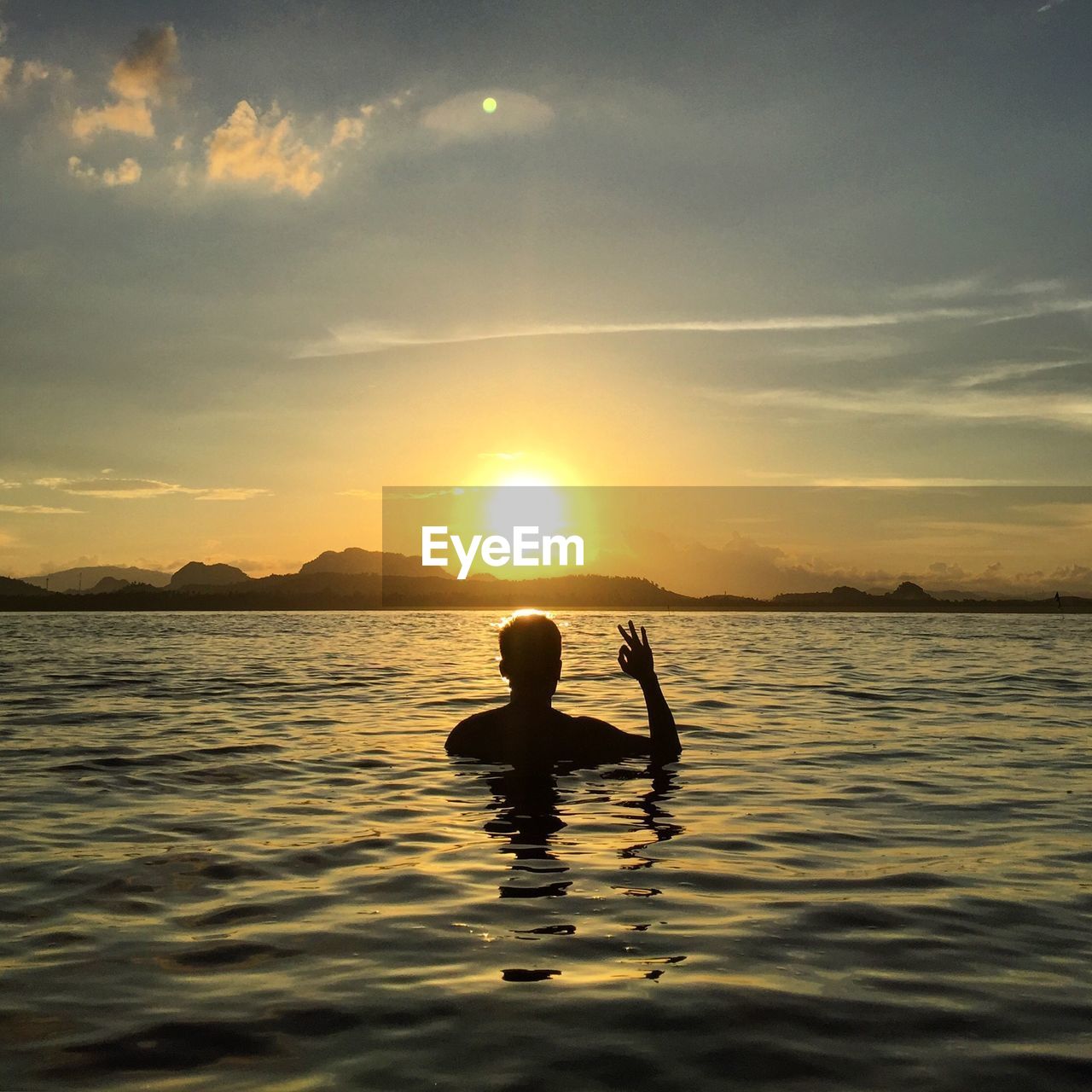 Silhouette man gesturing ok sign in sea against sky during sunset