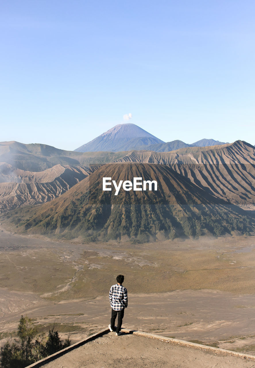 Rear view of man standing at volcanic landscape against clear sky