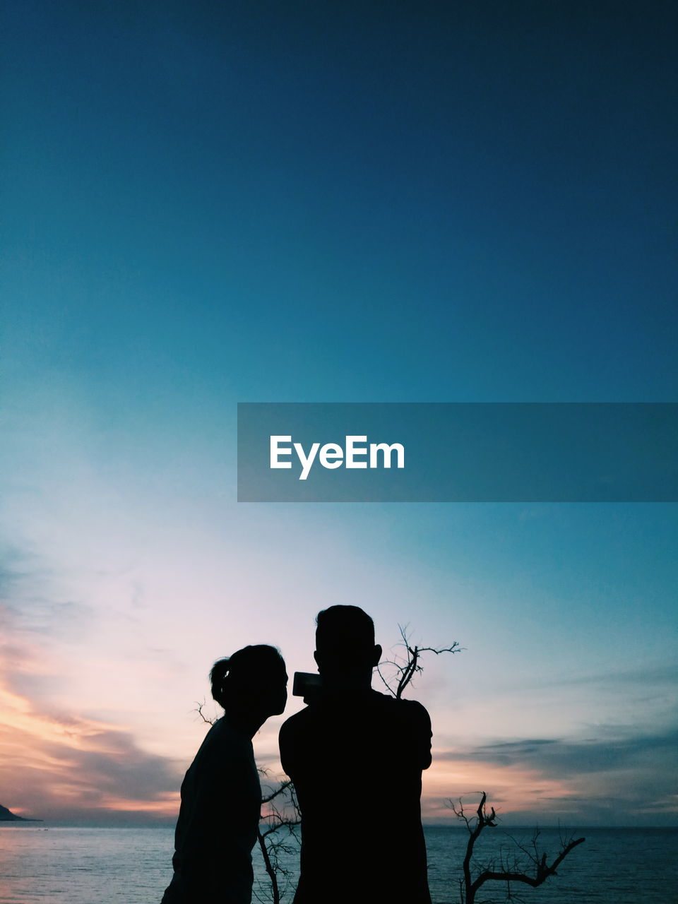 Silhouette couple standing at beach against blue sky