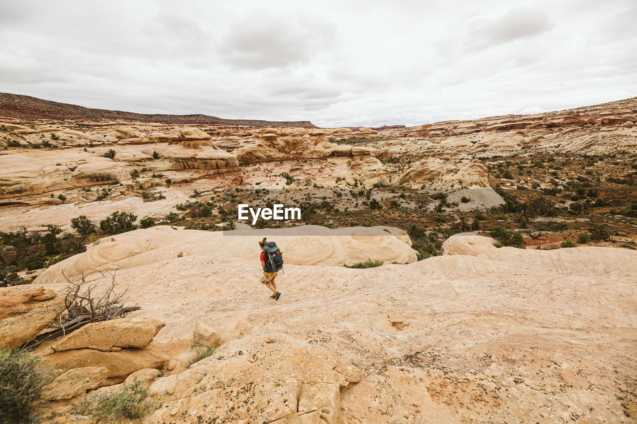 Female backpacker walks down a sandstone rock face in utah desert