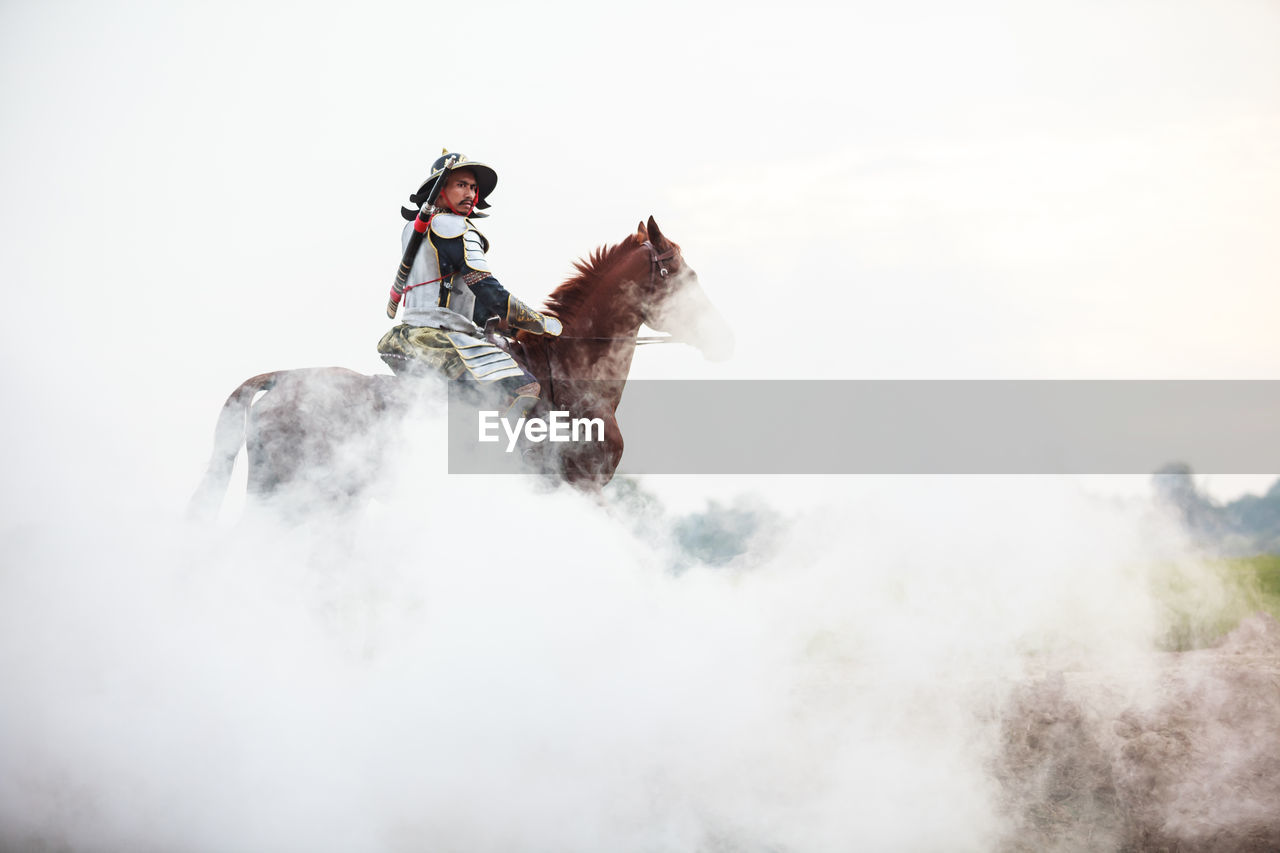 Low angle view of warrior riding horse in foggy weather