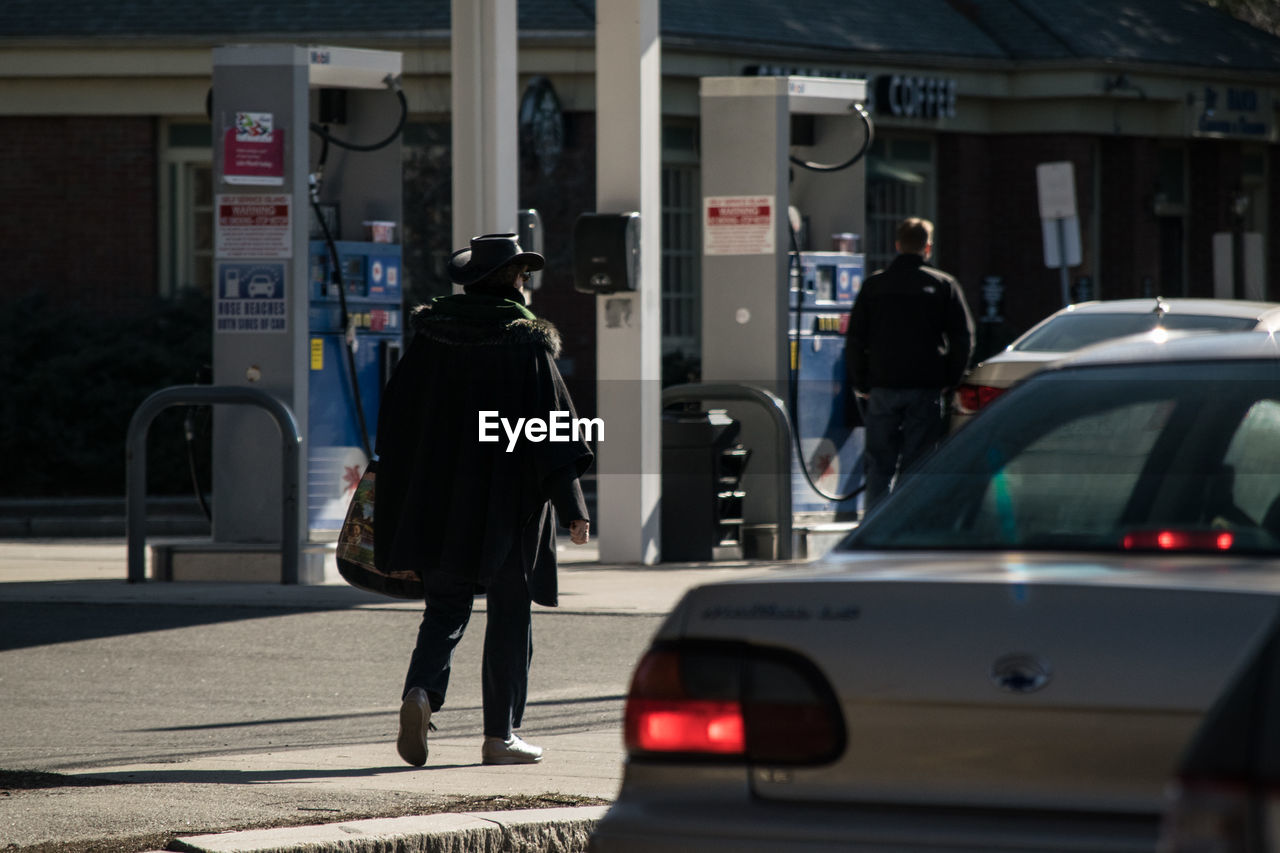 Rear view of people by cars at gas station