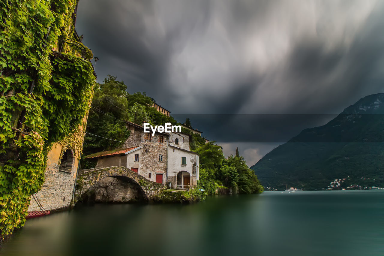 HOUSE BY LAKE AGAINST CLOUDY SKY