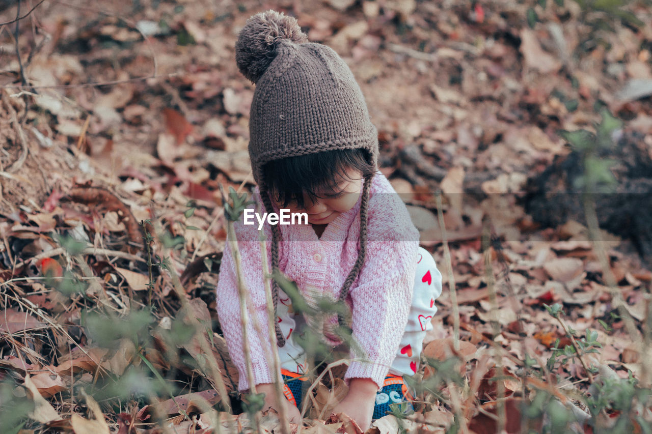 Cute baby girl crouching and playing with leaves during winter