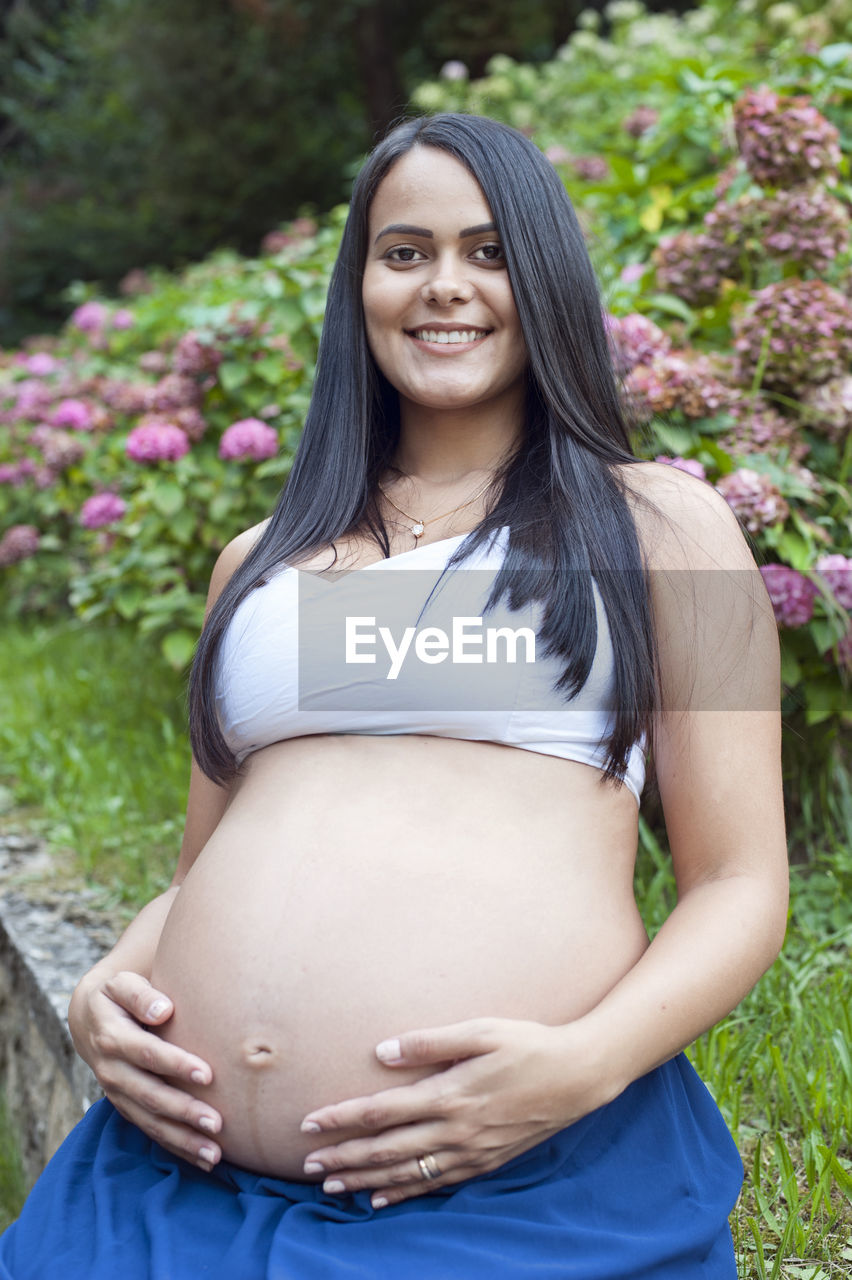 Young pregnant brazilian woman touching her belly in a garden person