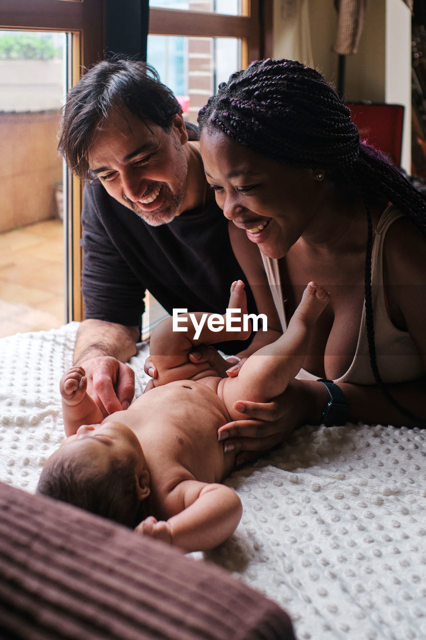 Caring african american mom changing diapers on infant lying on blanket with hispanic dad