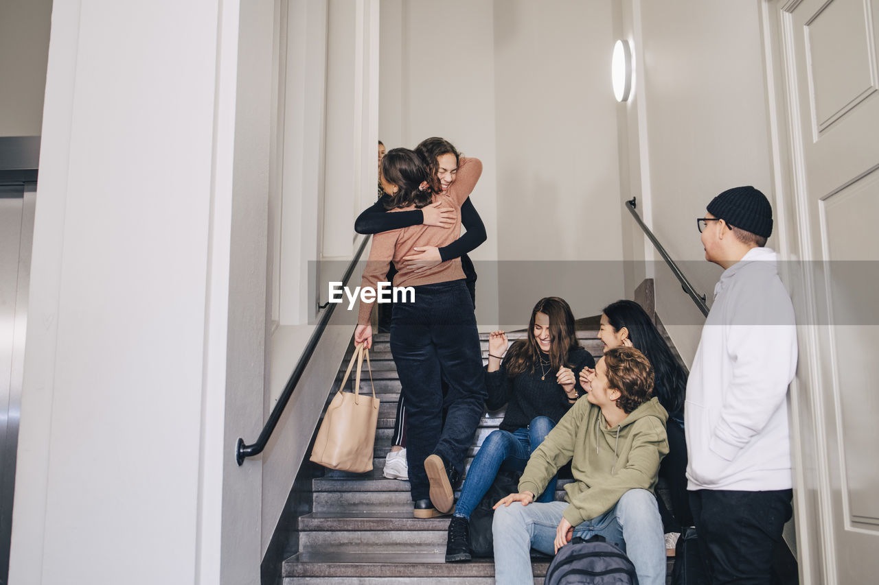 Teenagers looking female classmates embracing on steps at high school