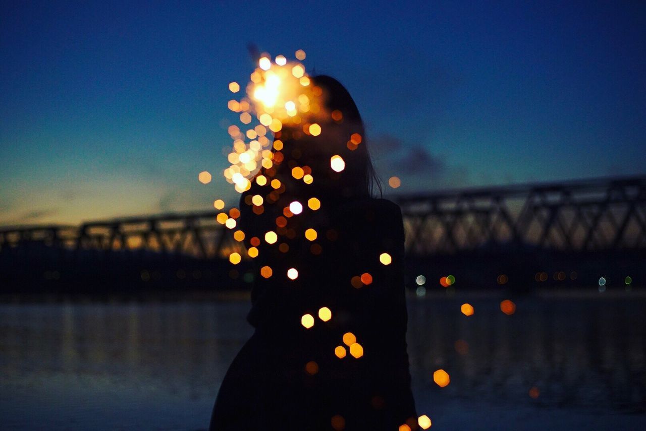 Digital composite image of silhouette woman with illuminated lights by lake at dusk