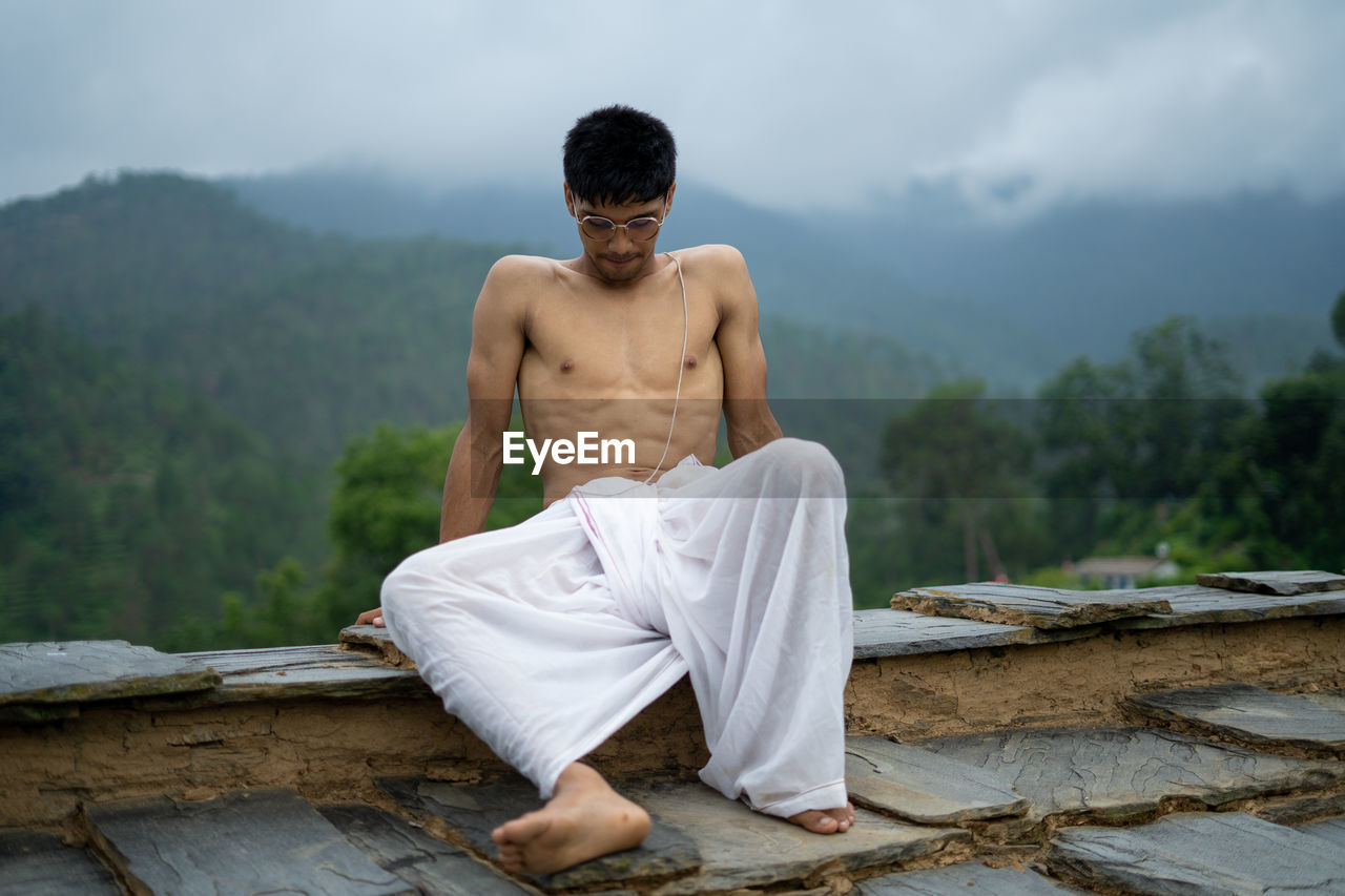 Full length of shirtless young man sitting outdoors