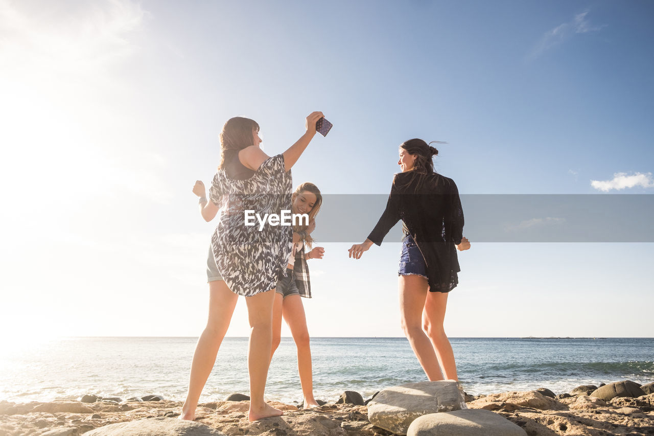 Low angle view of cheerful friends enjoying at beach against sky