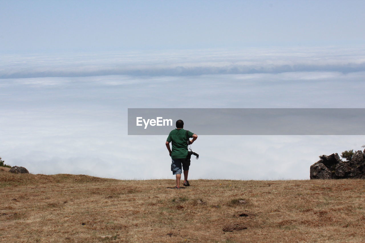 Rear view of man walking on field against sky