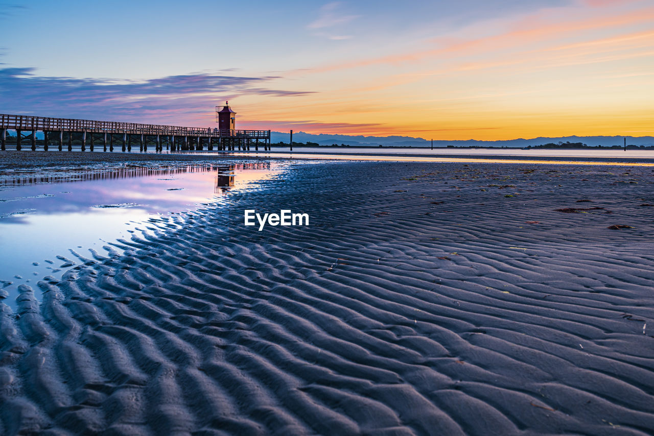 Sunrise over the sea. the lighthouse of lignano sabbiadoro and the games of sand and colors. italy