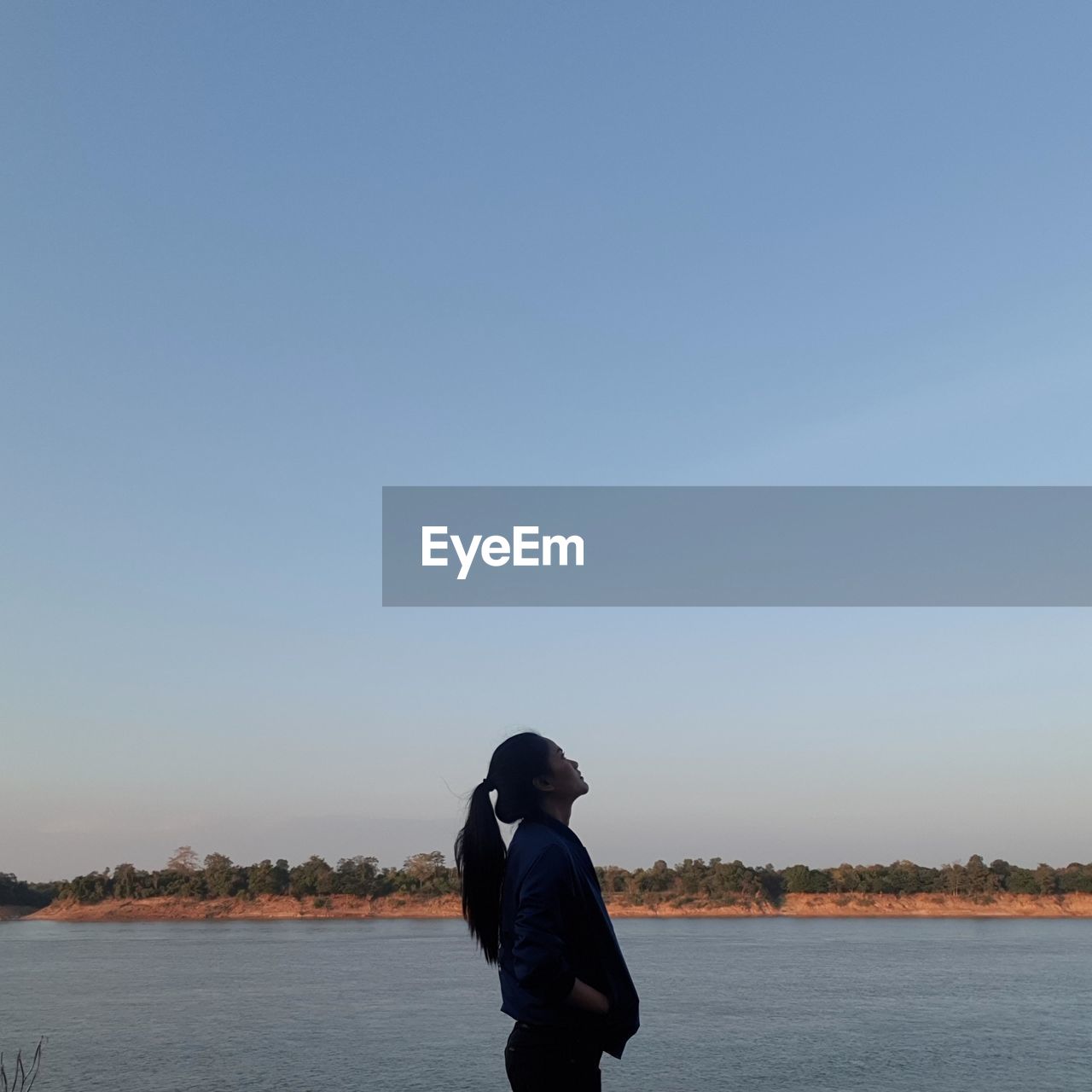 Side view of woman looking up against clear sky