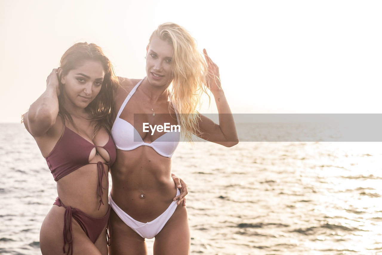 Portrait of sensuous female friends wearing bikinis standing at beach