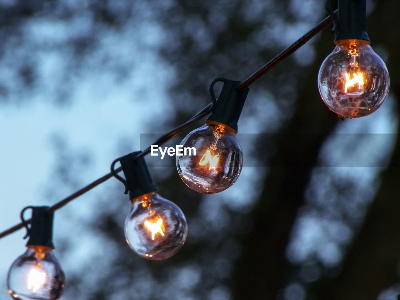 Low angle view of illuminated light bulbs against sky at dusk